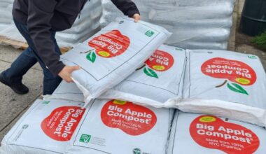 Someone picking up a large bag of Big Apple Compost from a pile on a pallet