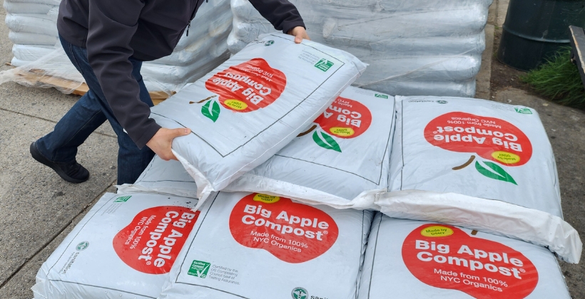 Someone picking up a large bag of Big Apple Compost from a pile on a pallet