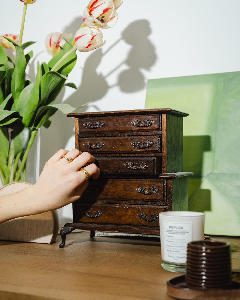 A hand opening a drawer of a miniature wooden dresser.