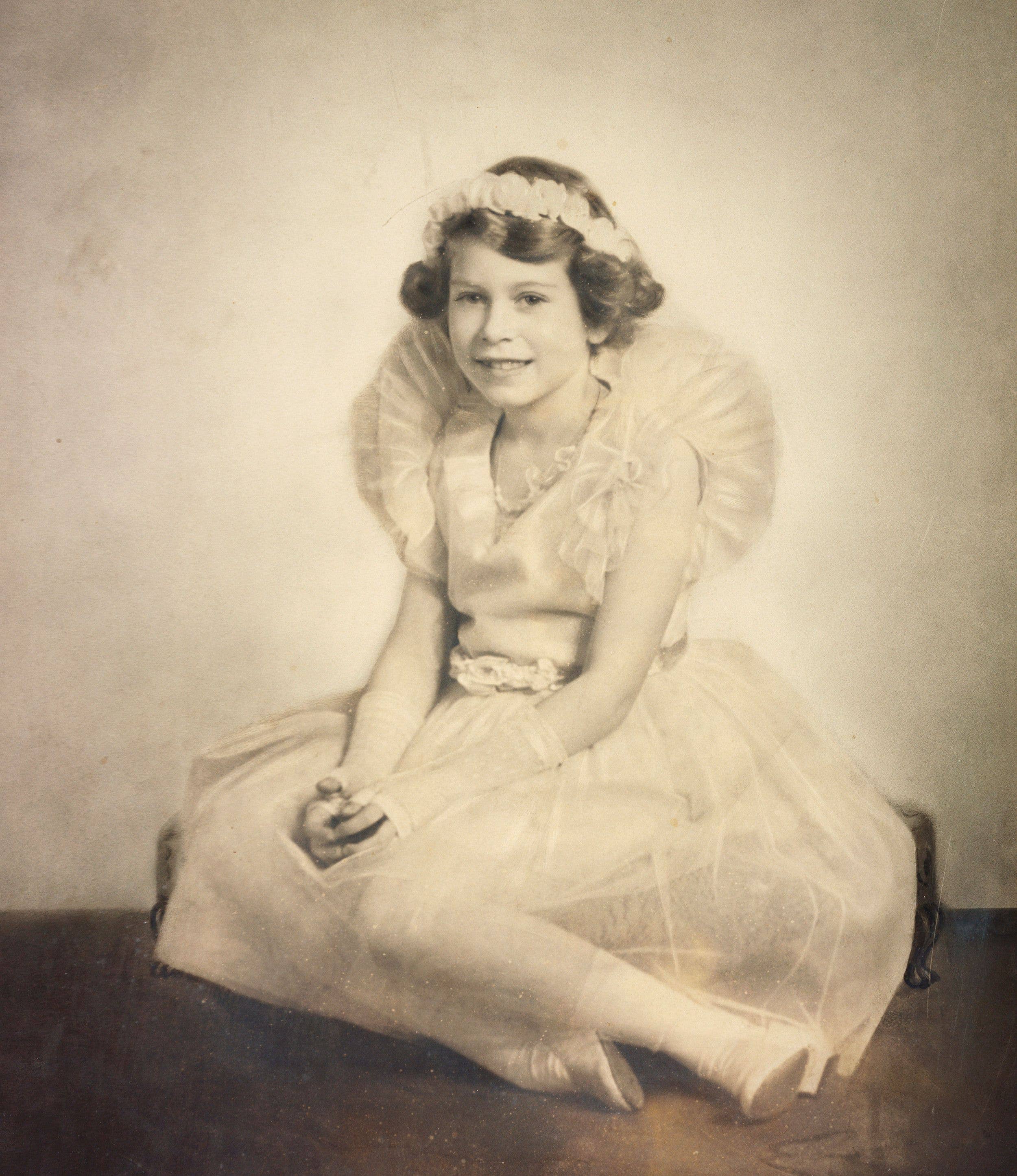 A young Princess Elizabeth sits while wearing her frilled bridesmaid dress for the wedding of her uncle Prince George, Duke of Kent to Princess Marina of Greece and Denmark in November 1934