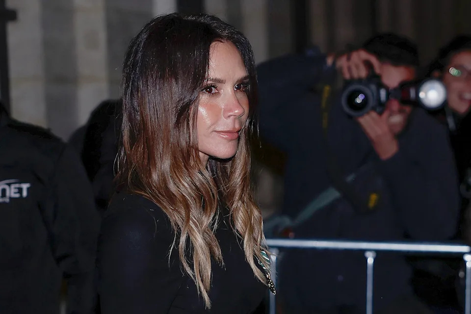 Victoria Beckham on a red carpet, wearing a sleek dress, surrounded by photographers