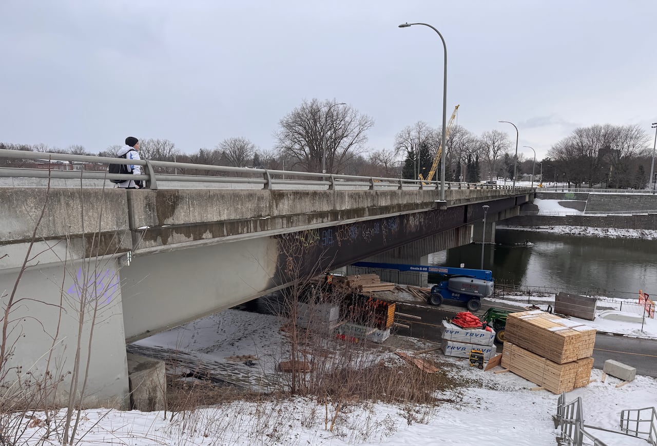 Construction materials are stagged under a bridge along a river.