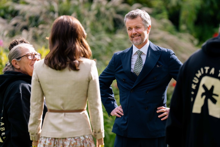 King Frederik puts his hands on his hips and smiles as he faces Queen Mary.