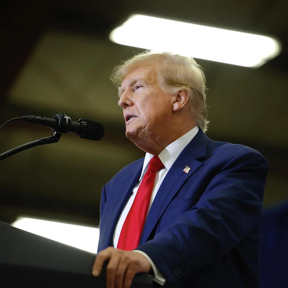 Donald Trump wears his signature navy suit and red tie combination while addressing a crowd.