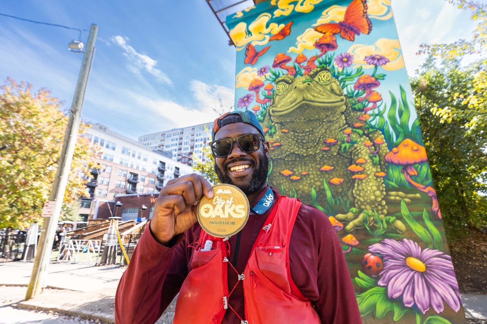 Runner showing a marathon medal in front of a colorful mural. City of Oaks Marathon