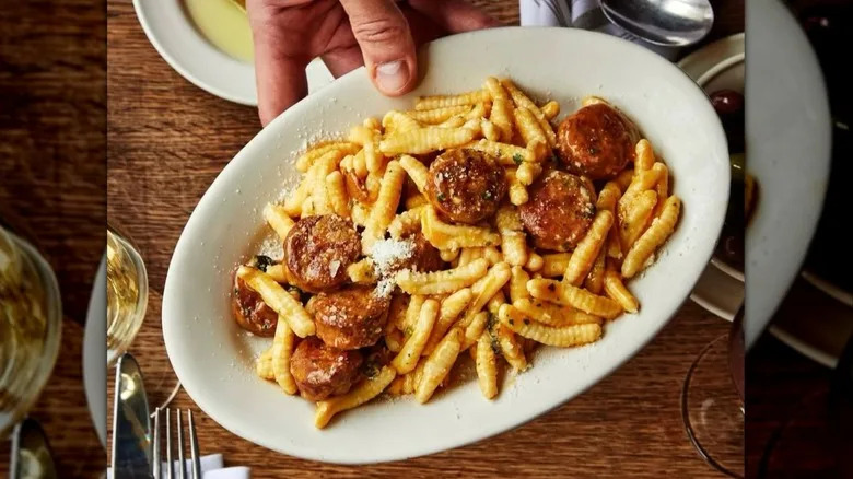 Pasta with sausage is held on an elongated plate.