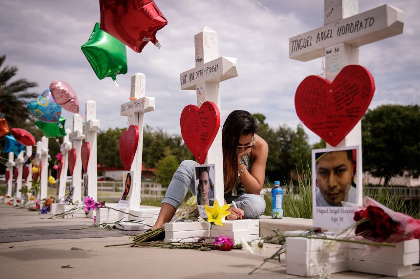 A woman writes a note at a memorial with wooden crosses for each of the 49 victims of the Pulse nightclub shooting in Orlando, Florida, in June 2016.