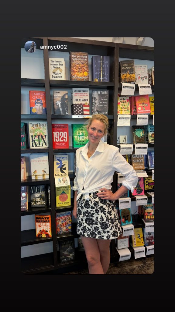 Woman standing in a bookstore in front of a shelf featuring the book "Strangers" by Belle Burden.