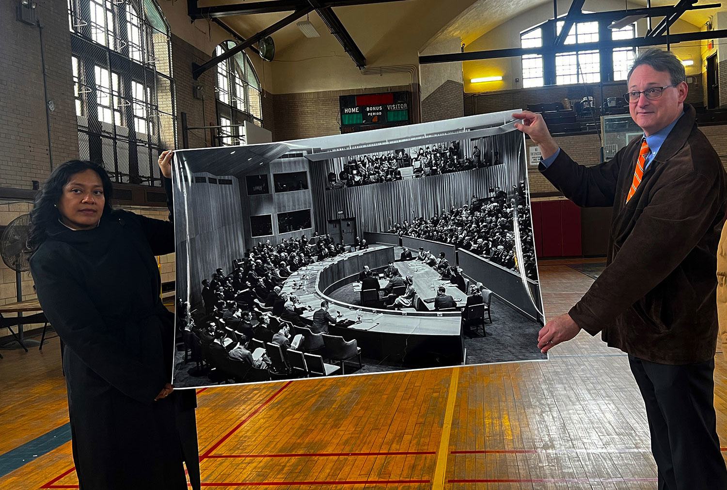 Two current-day employees of Lehman College hold a photograph of the UN Security Council from 1946 which once occupied the college's basketball court.  