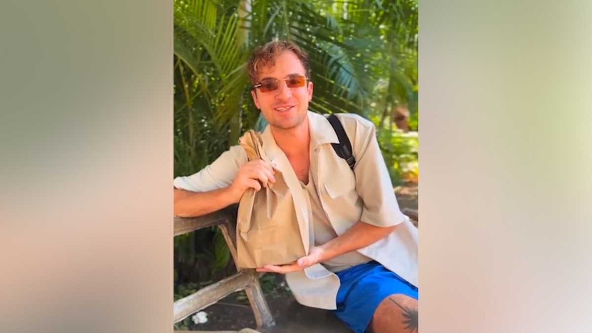 Kevin Droniak holding paper bag of food in front of palm trees in Jamaica.