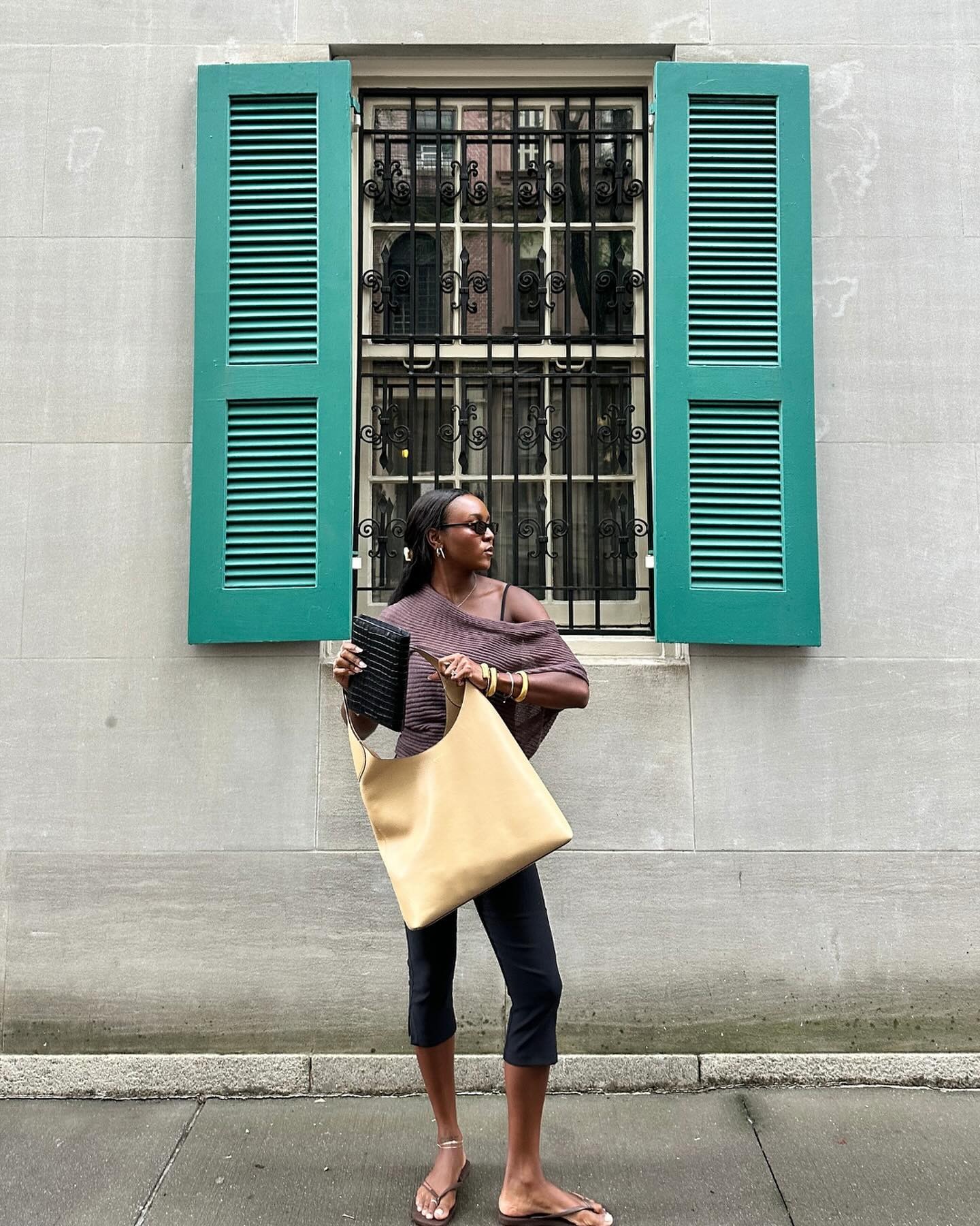 Woman wears sheer top, capari pants and carries yellow Coach bag