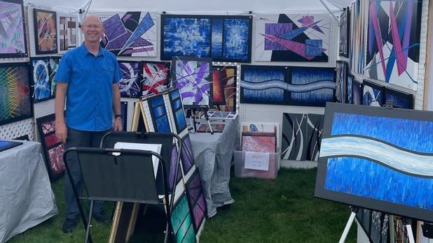 A man stands under a tent filled with various paintings
