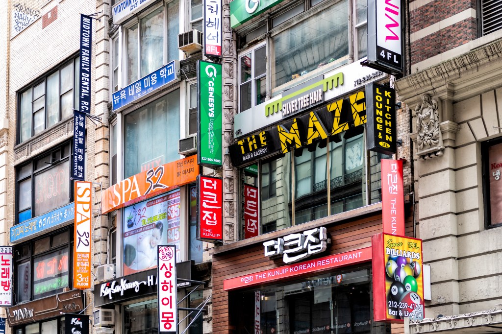 Street view of multiple stacked signs for businesses in Koreatown, New York City, including "The Maze Bar & Eatery," "The Kunjip Korean Restaurant," and "Space Billiards."