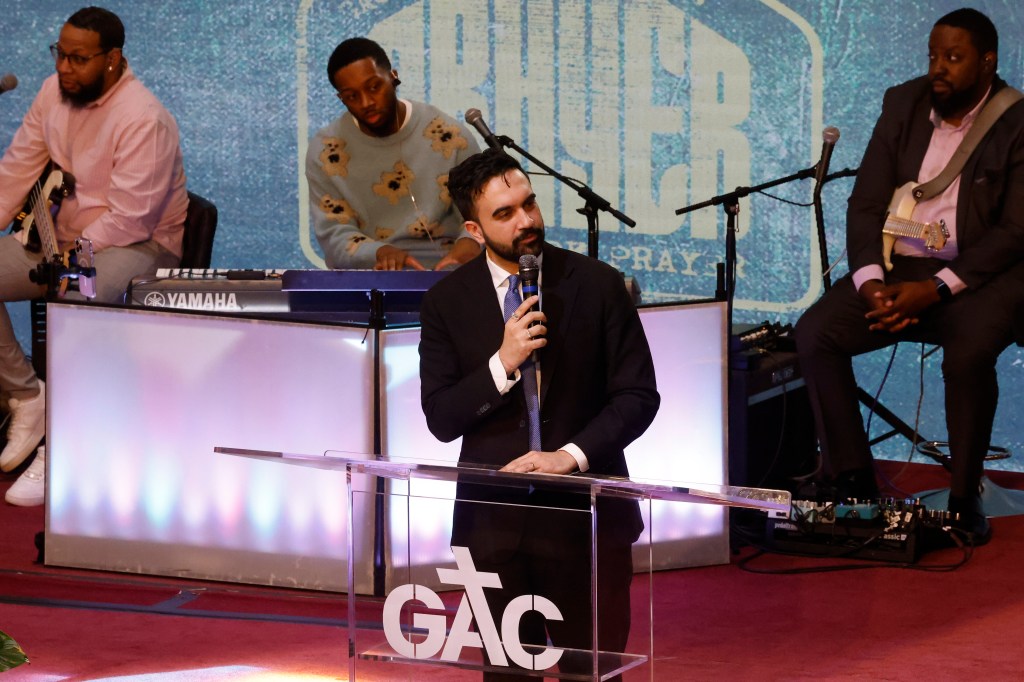 Zohran Mamdani speaks at a podium with a microphone.