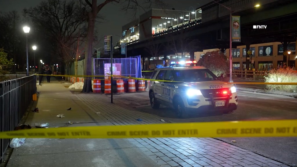 A police vehicle with flashing lights is parked at a crime scene blocked off by yellow "CRIME SCENE DO NOT ENTER" tape.