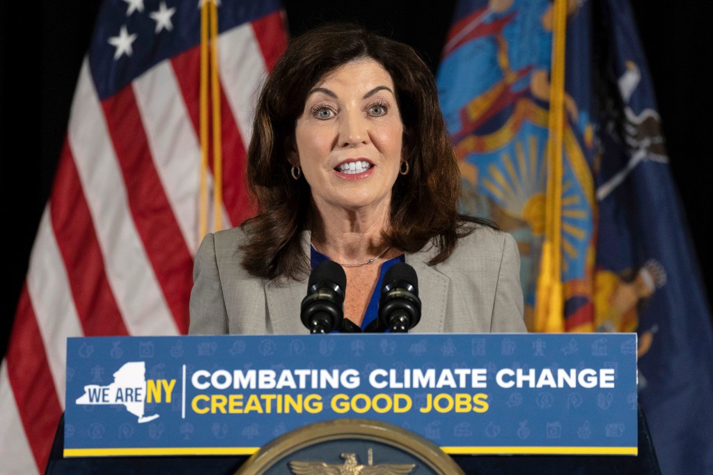 New York Gov. Kathy Hochul speaking at a press conference with "Combating Climate Change Creating Good Jobs" on the podium.