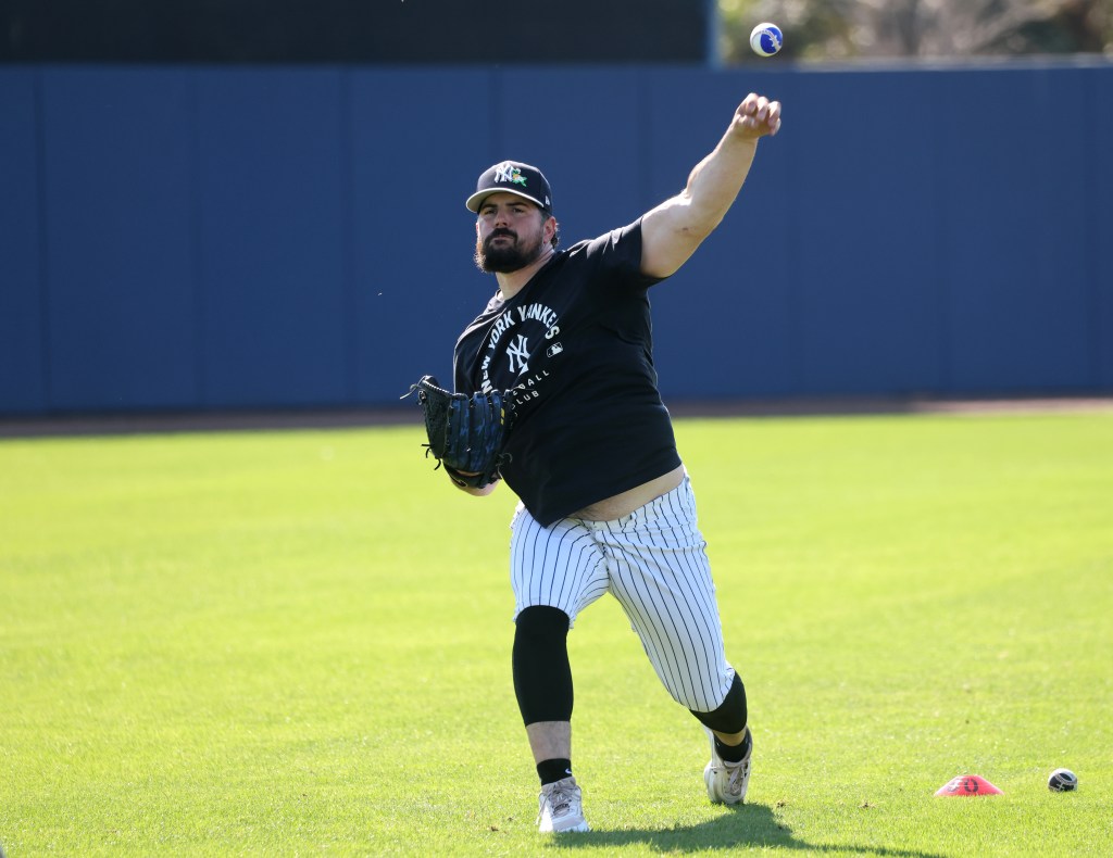 New York Yankees pitcher Carlos Rodón throwing a multi-colored ball in the outfield.