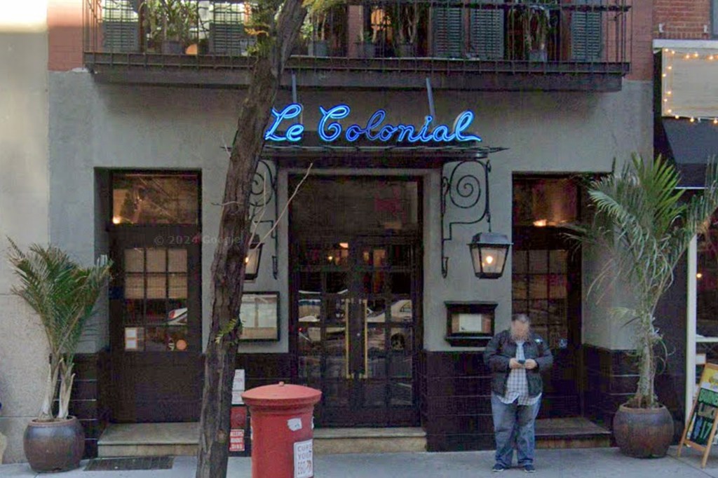 The exterior of the now closed Le Colonial restaurant on East 57th Street in New York, with a neon blue sign and a man looking at his phone.
