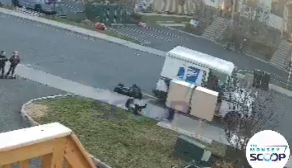 A low-quality, zoomed-out image shows a postal worker shoving a child near a mail truck and two large boxes.