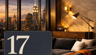 Sophisticated Manhattan penthouse living room featuring charcoal velvet sectional, blackened steel windows, walnut console, brass lighting, and twilight skyline views