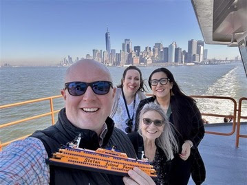 A group of four people on a ferry with the New York City skyline in the background.