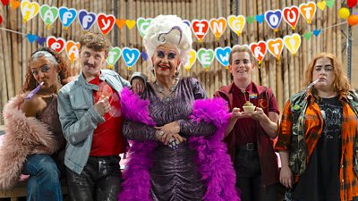 Five people in party outfits stand in front of bunting that reads: "Happy Coming Out Party."