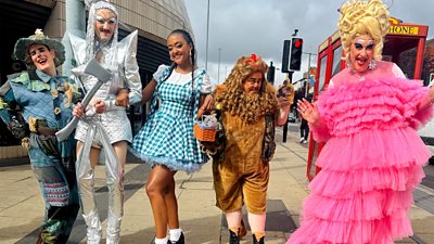 Five people in costumes from the Wizard of Oz walk along a highstreet. 