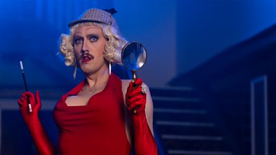 Close-up of Dickie (Phil Dunning) dressed in drag as Sherlock Holmes. 