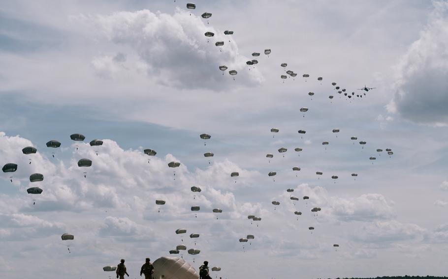 Paratroopers of the 82nd Airborne Division descend from the sky under parachutes with a plane flying overhead.