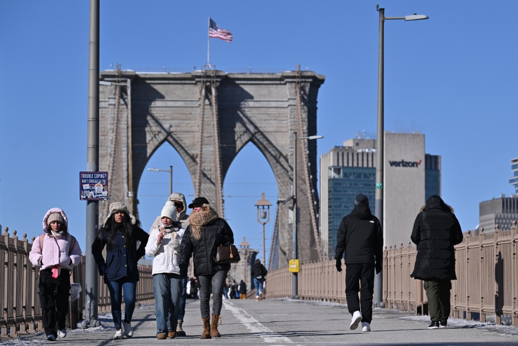 People bundled in winter clothes walk on the Brooklyn Bridge pedestrian walkway.