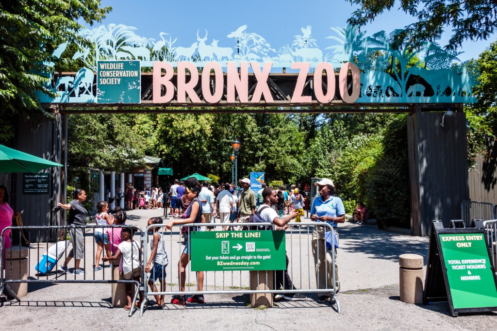 Entrance to the Bronx Zoo with a ticket taker, visitors, and a "Skip the Line" sign.