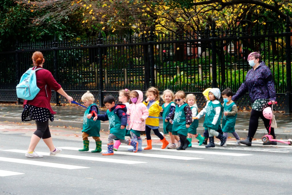 Two teachers helping pre-school children cross the street.