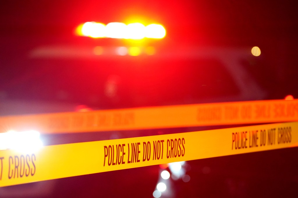 Police tape with the words "POLICE LINE DO NOT CROSS" across it at a crime scene at night.