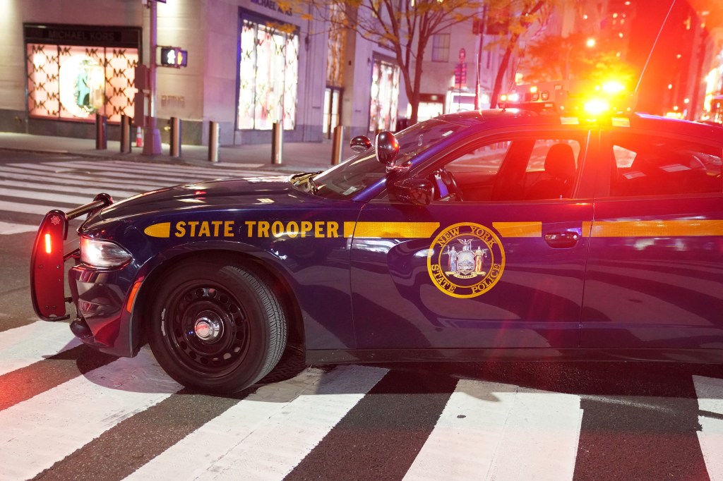 New York State Police vehicle with emergency lights flashing, parked on a crosswalk in New York City.