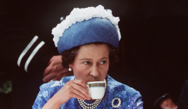 Queen Elizabeth wearing a blue dress and hat drinking tea