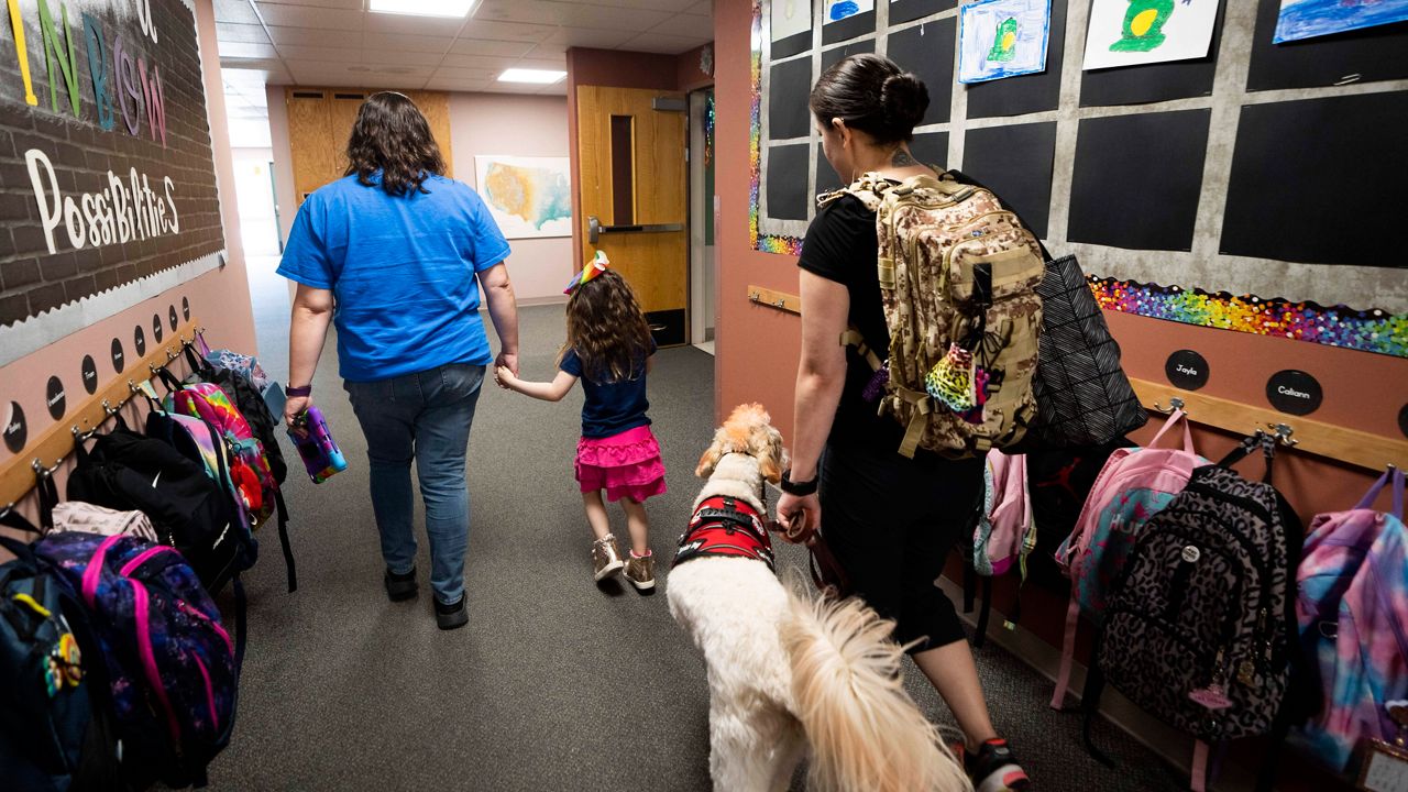 A long-term substitute special education teacher walks with a student as her mother follows with service dog