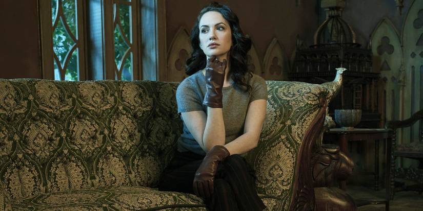 Katie Siegel sitting on an upholstered couch with gloves looking pensive in The Haunting of Hill House.