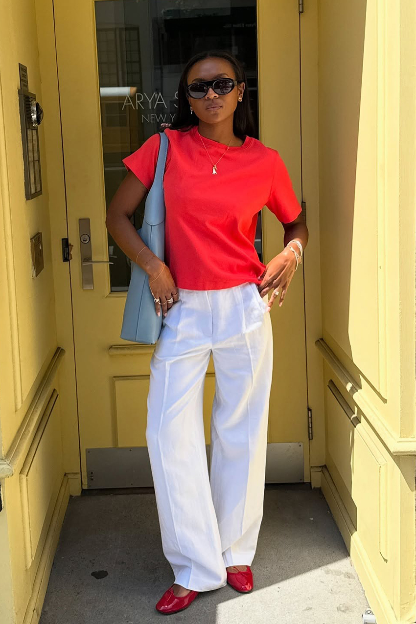 a woman wearing a red baby tee, white pants, red flats, and blue bag