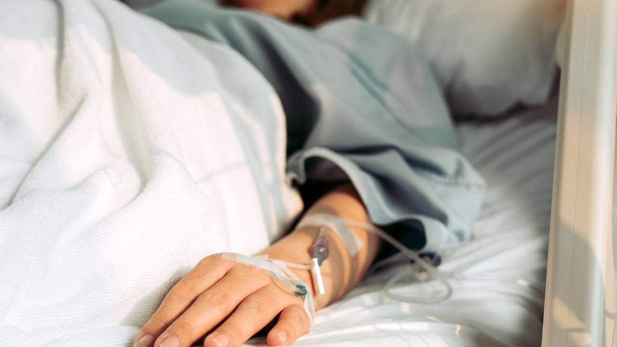 Inside a hospital room, a woman lies in bed appearing unwell