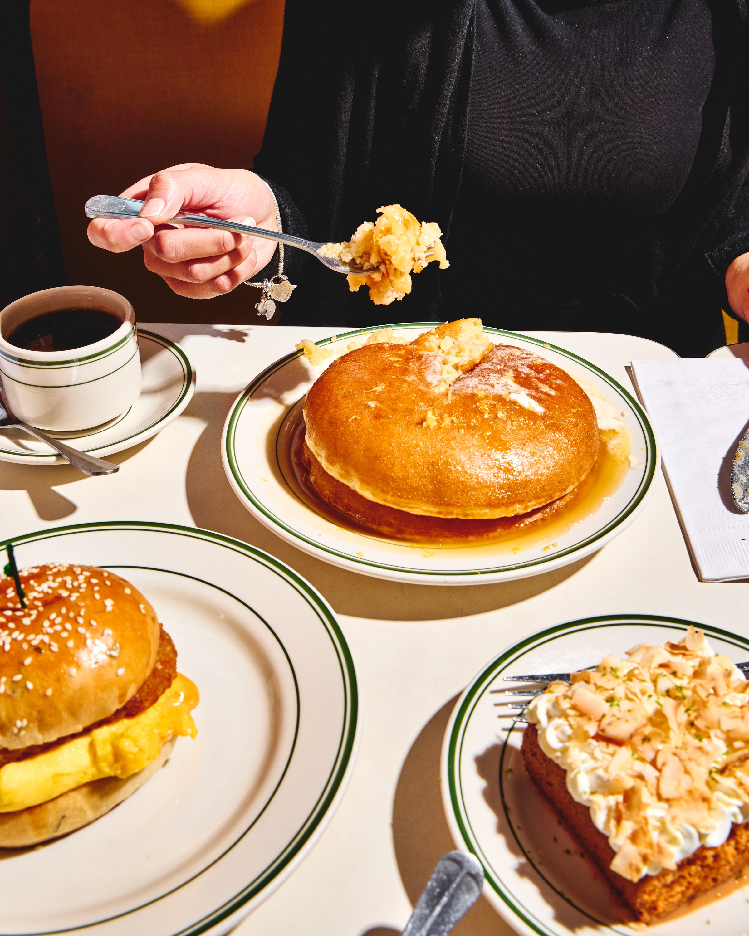 A diner takes a forkful of a fluffy pancake, alongside other diner dishes.