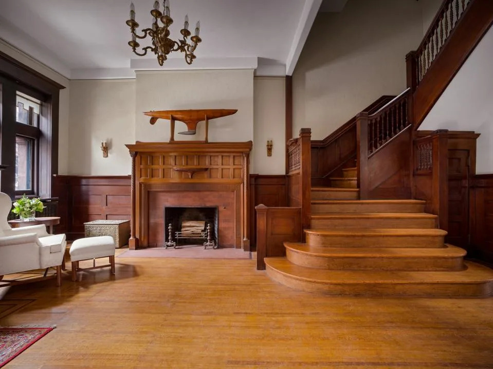 living room of Brooklyn Brownstone with wood-panelled fireplace suround and wooden staircase