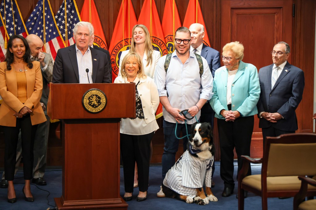 Bruce Blakeman signs a bill restricting how animals can be tethered outdoors, with several people and a Bernese Mountain Dog in a pinstriped shirt present.