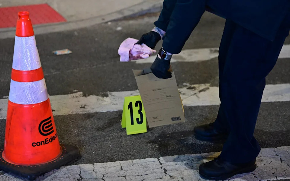 Police officer collects blood-stained hat on Humboldt Street after fatal shooting of 7-month-old baby in Brooklyn, New York