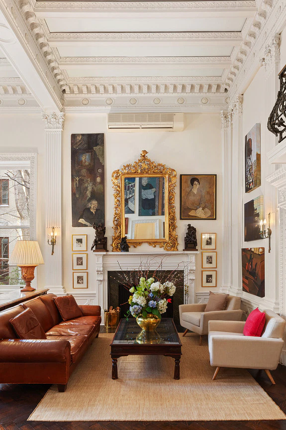 Elegant living room with ornate gold mirror, leather sofa, armchairs, and decorative paintings on walls.