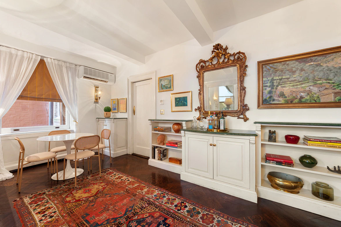 Stylish living room with white furniture, ornate mirror, colorful rug, and paintings, filled with natural light.