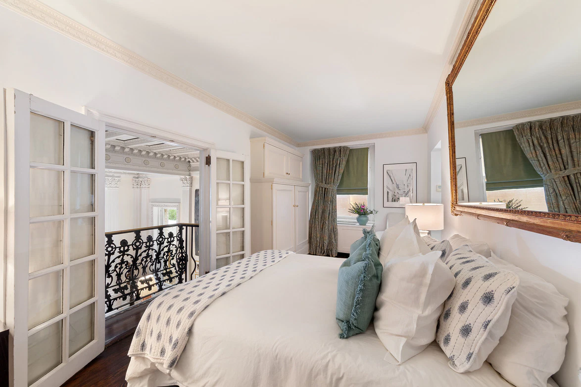 Elegant bedroom with plush pillows, large mirror, and French doors leading to a balcony with ornate railing.