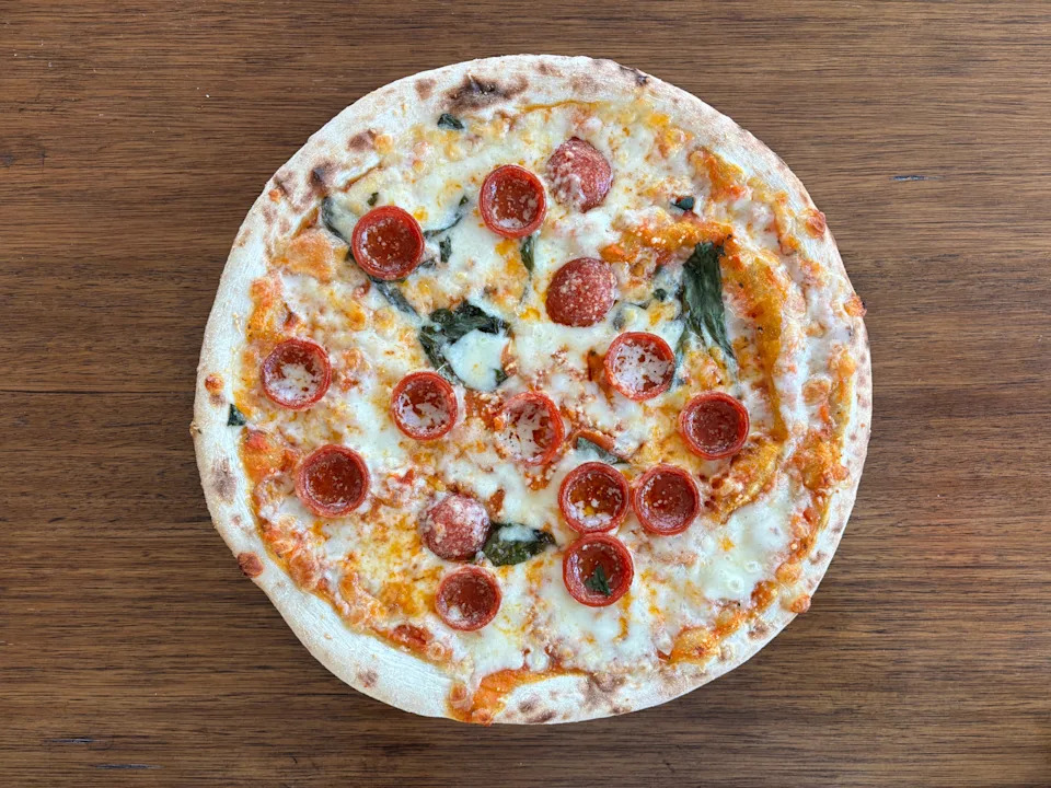 Pepperoni pizza with melted cheese and basil on a wooden table