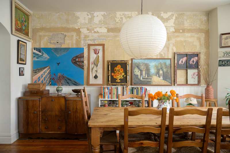 Dining area featuring a wooden table, chairs, and a variety of colorful artwork on the walls. A large paper lantern hangs above.