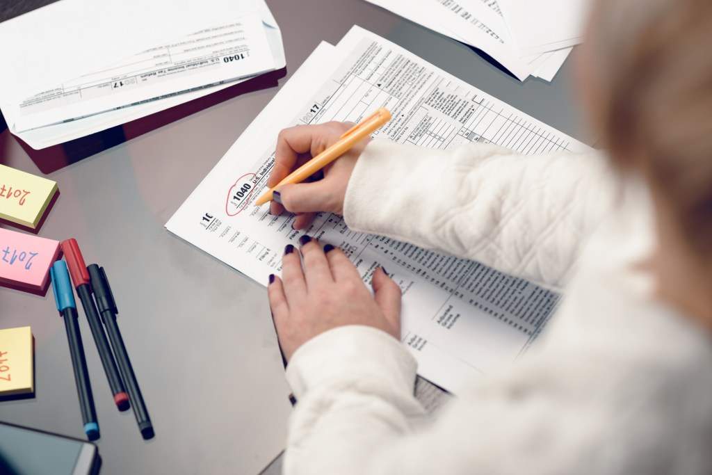 A woman's hands work on a US 1040 Individual Income Tax Return form.
