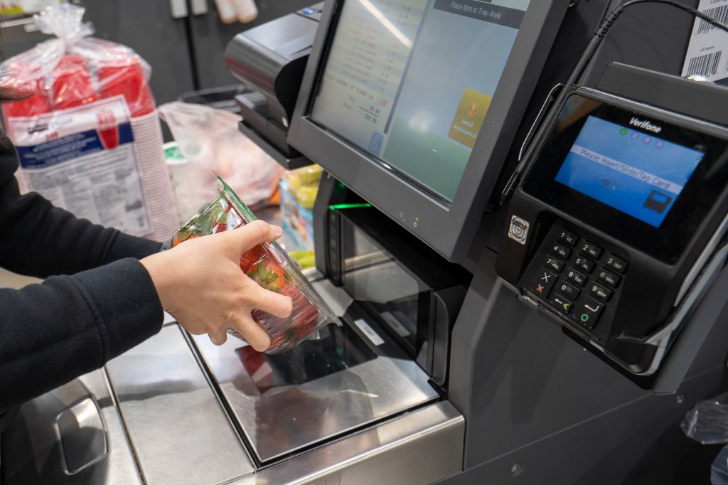 A shopper scans a box of strawberries at a self-checkout lane in a Costco store.
